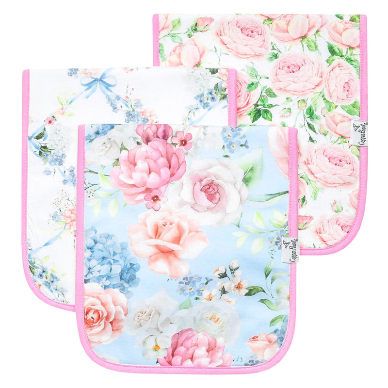 Three baby bibs with rounded corners, featuring a soft pastel floral print in pink, blue, and white, with pink piping borders. The bibs are arranged overlapping on a clean white background.