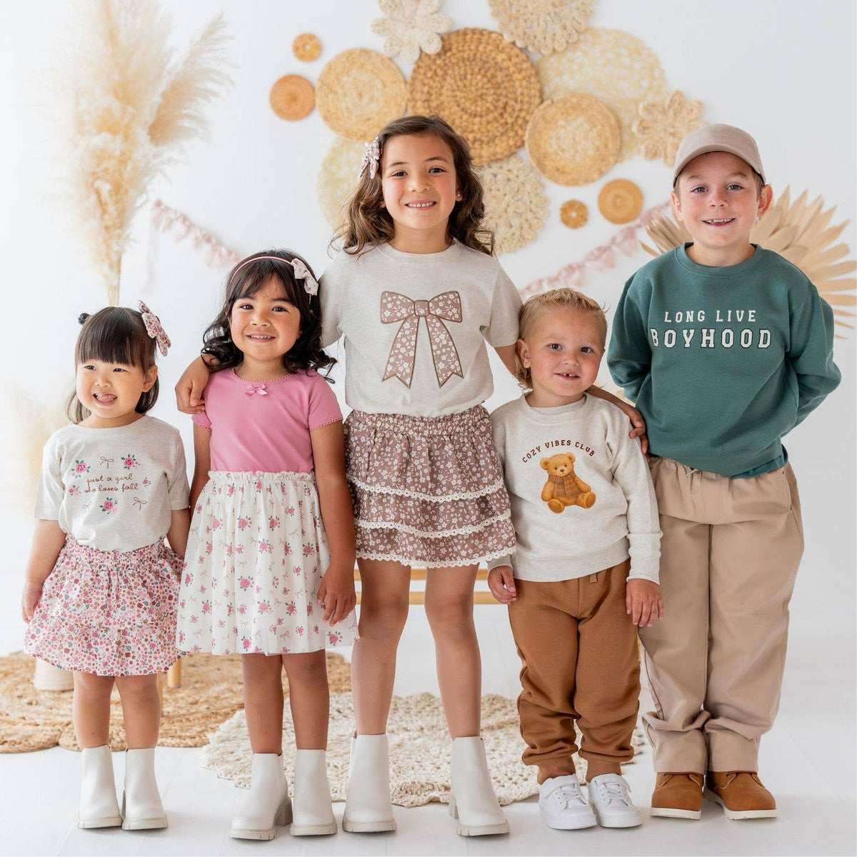 Five children standing together in front of a decorative floral backdrop