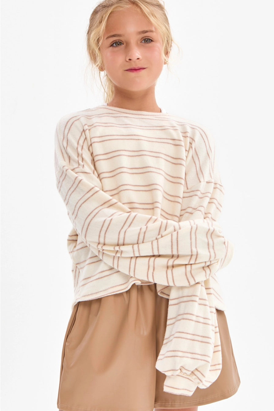A girl wearing a cream and taupe fine horizontal stripe brushed knit pullover top with a crew neckline, long sleeves with slightly flared cuffs, and a relaxed fit.