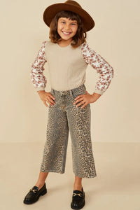 Child wearing a patterned top, leopard print pants, and a brown hat on a beige background