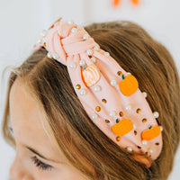Pink headband with pumpkins and pearls on a child's head against a white background