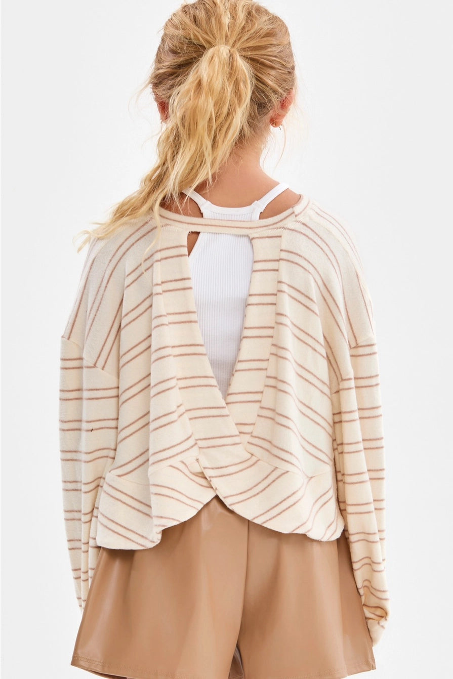 A girl wearing a cream and taupe fine horizontal stripe brushed knit pullover top with a crew neckline, long sleeves with slightly flared cuffs, and a relaxed fit.