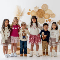 Children wearing stylish clothing in front of a decorative wall with flowers and balloons.
