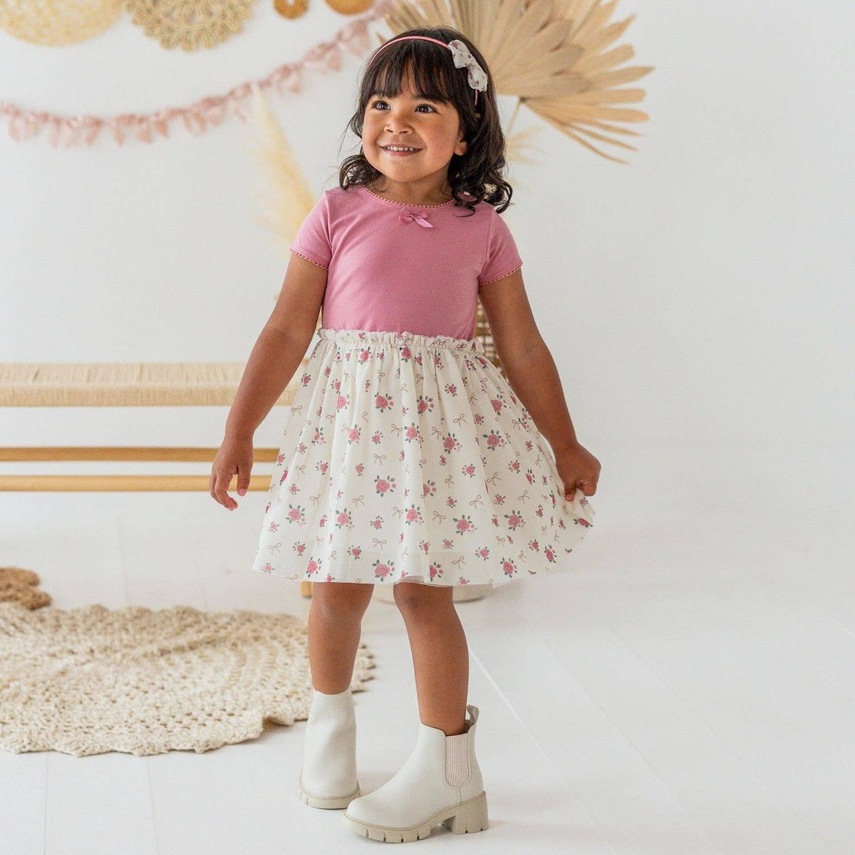 Young girl in a pink top and floral skirt standing in a room with decorative elements.