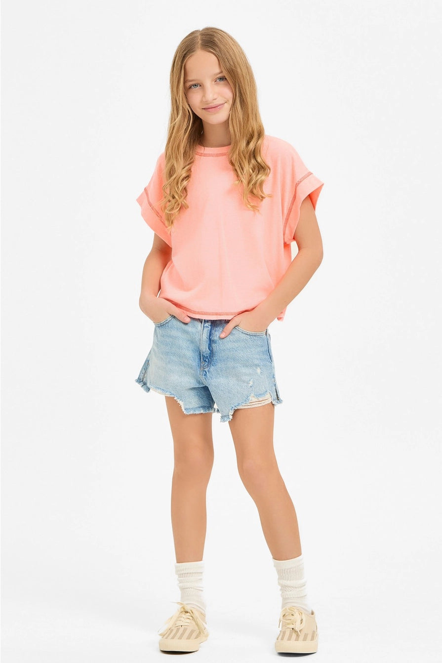 Young girl wearing a pink oversized shirt and denim shorts on a white background